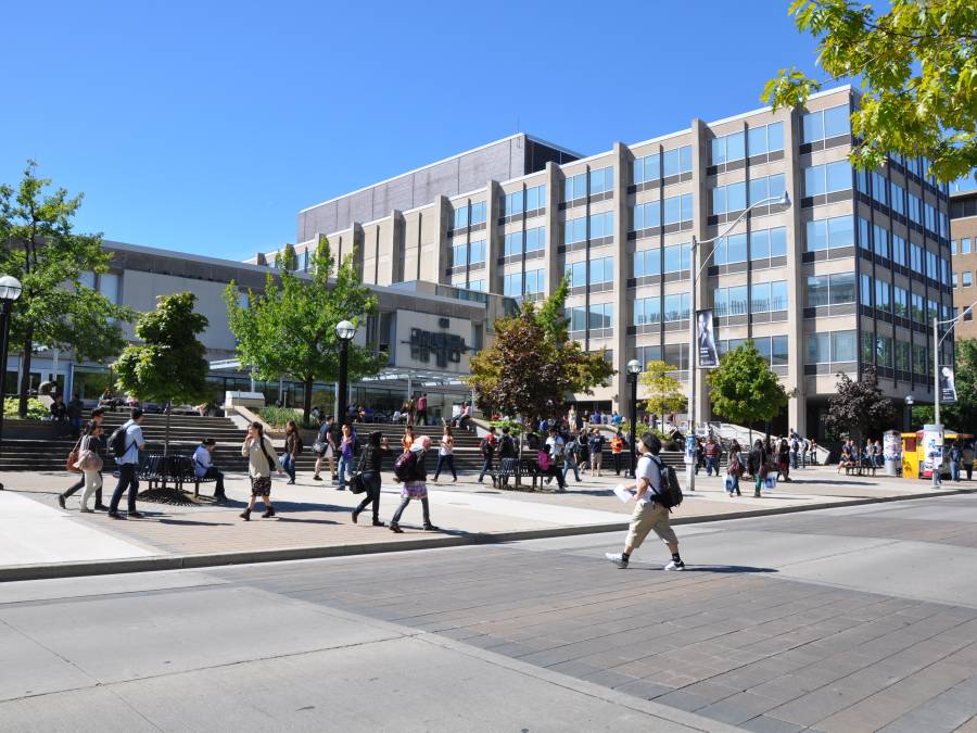 Outside of Sidney Smith building on a summer day with people walking across the road in front of it