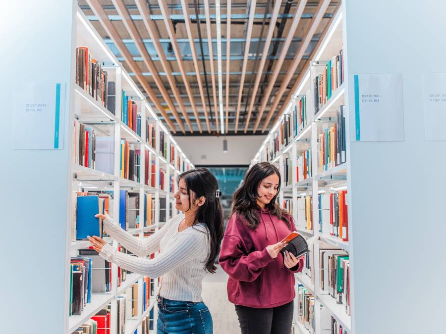 Two students looking at books in library stacks.