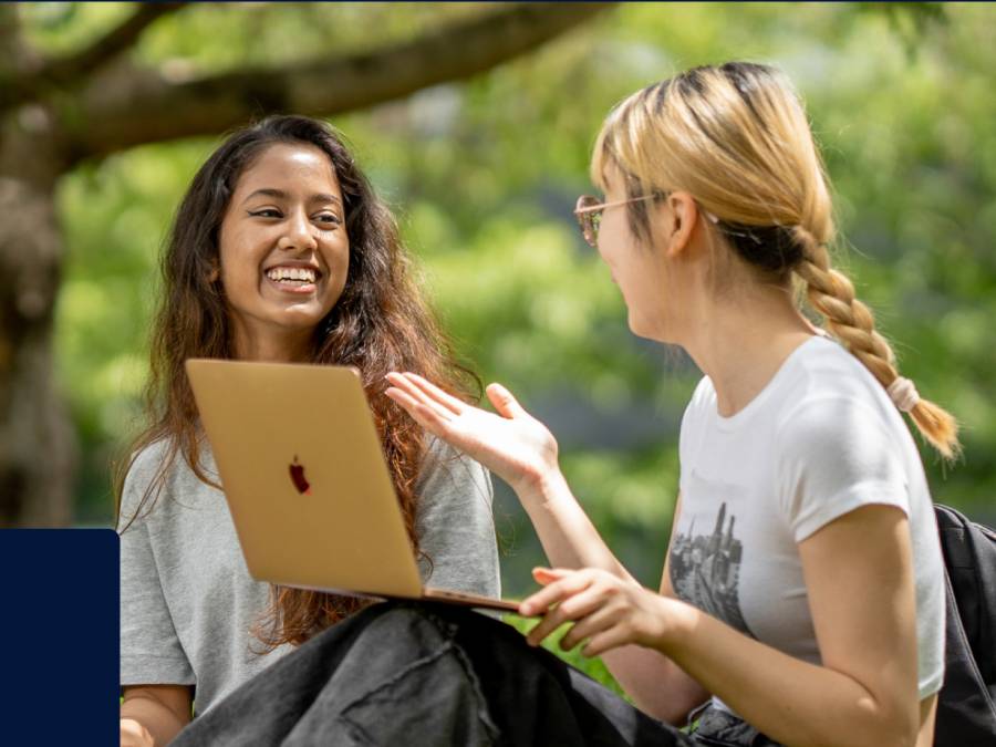 Two students chatting outside in front of a laptop.
