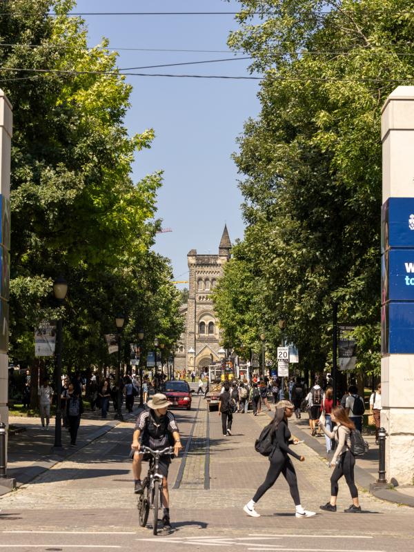 Entrance to U of T front campus with people talking in front of the U of T entrance gates and someone riding a bicycle