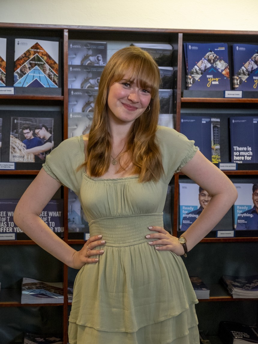 U of T student posing in front of viewbooks
