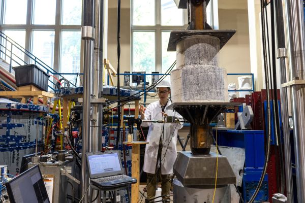Student pouring concrete into forms in a lab with a lot of industrial equipment