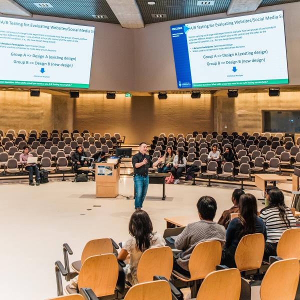 Professor speaking in a classroom surrounded by seats and students