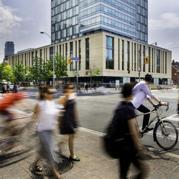 Pedestrians and cyclists move through a busy intersection on a bright day
