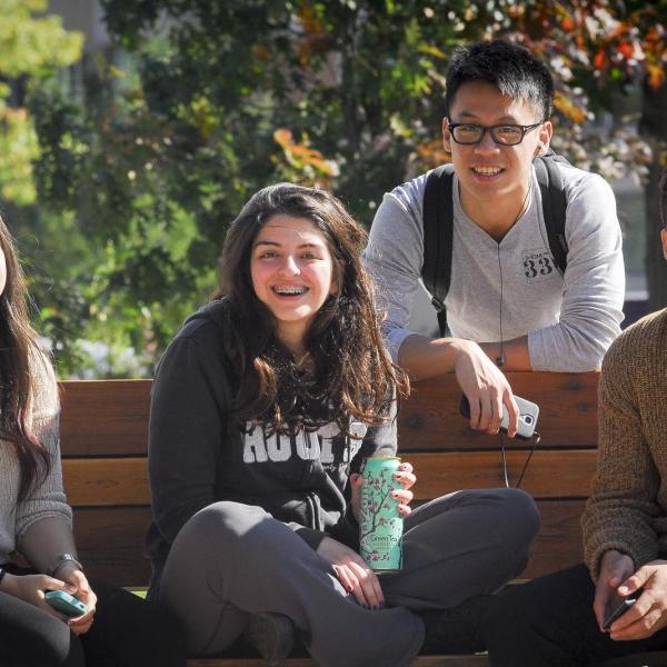 Four students sitting on a bench and smiling for the camera.