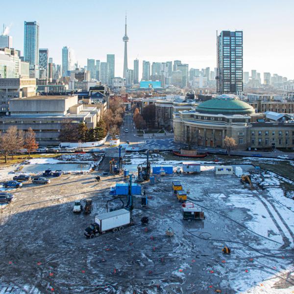 View of front campus at the University of Toronto in winter, with construction equipment and the Toronto skyline in the background